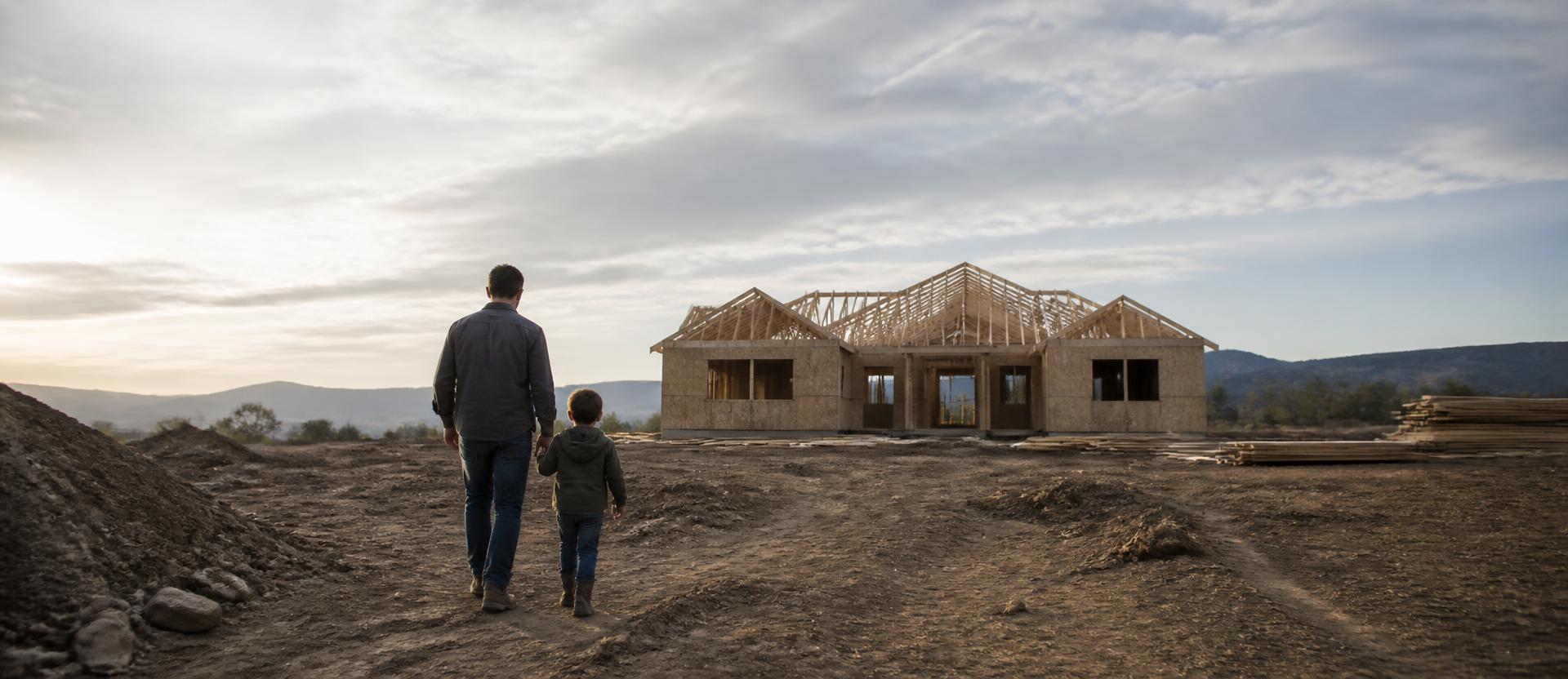 A parent and child walking across a homesite toward their house under construction